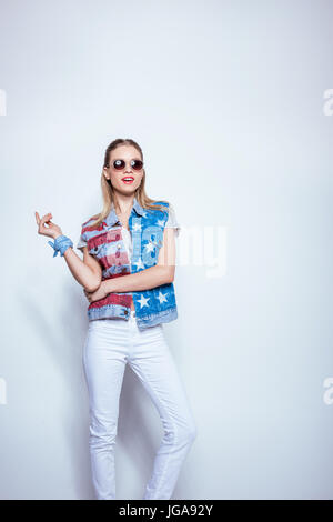 Attraente ragazza bionda in occhiali da sole indossando giubbotto in denim con noi bandiera e in posa di studio Foto Stock