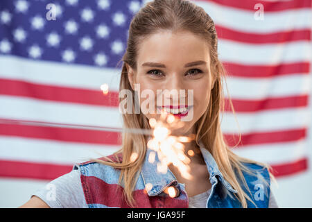 Ritratto di donna felice azienda sparkler con bandiera americana dietro, Independence Day celebrazione Foto Stock