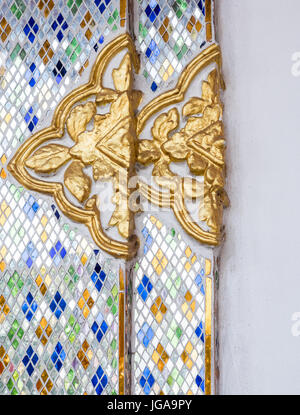 Doppia in stucco con motivi floreali che decorate con mosaici in vetro sul muro bianco della Chiesa thai. Foto Stock