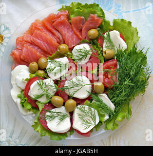 Un semplice utile e gustosi snack sotto la vodka sul tavolo del villaggio. Salmone affumicato, pomodori con mozzarella e insalata fresca Foto Stock