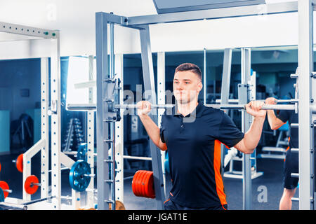 Montare il giovane uomo il sollevamento barbells cercando focalizzata, lavorando in una palestra Foto Stock