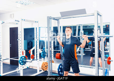 Montare il giovane uomo in sollevamento sportswear barbells cercando focalizzata, lavorando in una palestra Foto Stock