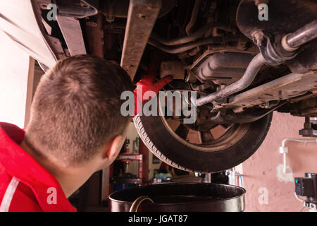 Autofficine in uniforme di operare sotto un auto sollevato con le attrezzature di lavoro per la riparazione e di diagnosi automatica del servizio di riparazione Foto Stock