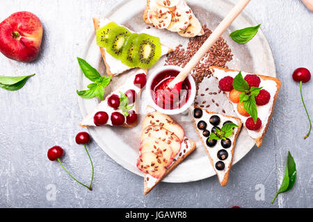 Toast di frutta su sfondo grigio. Colazione sana. Pulire mangiare. dieta concetto. grano fette di pane con formaggio cremoso e diversi tipi di frutta, bacche, vedere Foto Stock