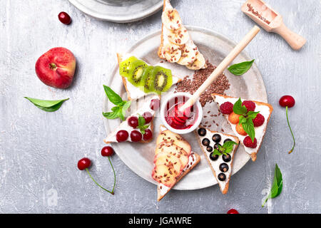 Toast di frutta su sfondo grigio. Colazione sana. Pulire mangiare. dieta concetto. grano fette di pane con formaggio cremoso e diversi tipi di frutta, bacche, vedere Foto Stock