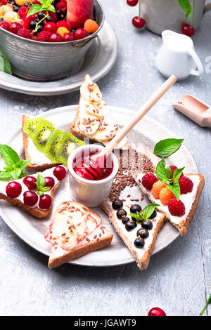 Toast di frutta su sfondo grigio. Colazione sana. Pulire mangiare. dieta concetto. grano fette di pane con formaggio cremoso e diversi tipi di frutta, bacche, vedere Foto Stock