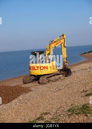 Un piccolo giallo cingolato escavatore cingolato lavorando su una spiaggia per spostare shingle, UK. Foto Stock