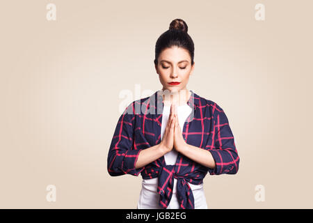 Giovani brunete donna pratica lo yoga, tenendo le mani in namaste e tenere gli occhi chiusi. Ragazza caucasica meditando in ambienti chiusi, pregando per la pace e lo Foto Stock