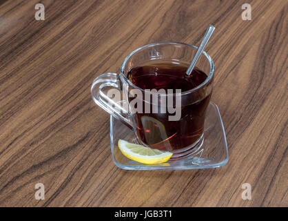 Bicchiere di vetro di tè serviti con una fetta di limone su uno sfondo di legno Foto Stock
