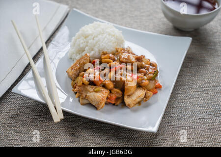 Lastra di Kung Pao pollo su piastra bianca con bacchette. Foto Stock