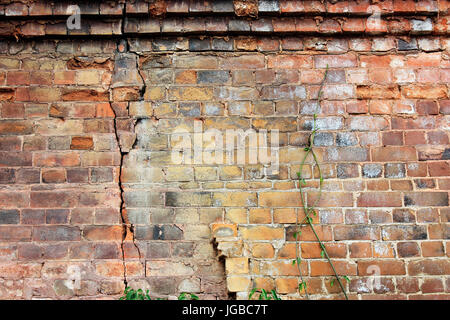 Vista ravvicinata di incrinato edificio vecchio muro di mattoni con mattoni erosi in cima, concetto di sfondo Foto Stock