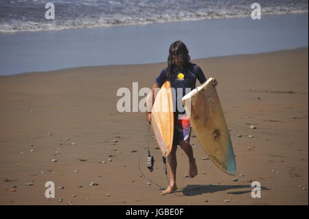 Surfista maschio cammina indietro lungo la spiaggia con la tavola da surf rotto Foto Stock