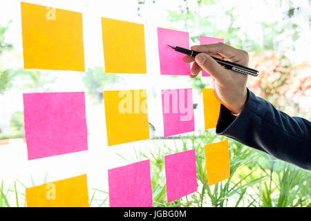 Immagine ravvicinata di mani di donna incollaggio note adesive sulla parete di vetro in office Foto Stock