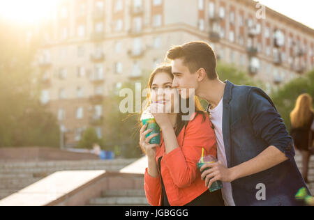 Gli adolescenti bere frutta fresca da bicchieri. Sussurra parole di gara nel suo orecchio. Un paio di amore su una data. Il romanticismo del primo amore. Foto Stock