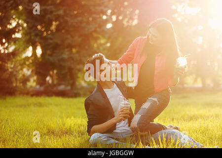 Un amorevole coppia di adolescenti. Improvviso picnic nel parco al tramonto. Teens bevande analcoliche, seduto sul prato. Egli abbraccia il suo. Ella corse la sua testa Foto Stock
