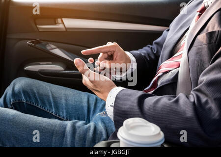 Giovane imprenditore bello lavorare nel retro della vettura e utilizzando un tablet o smart phone. Foto Stock