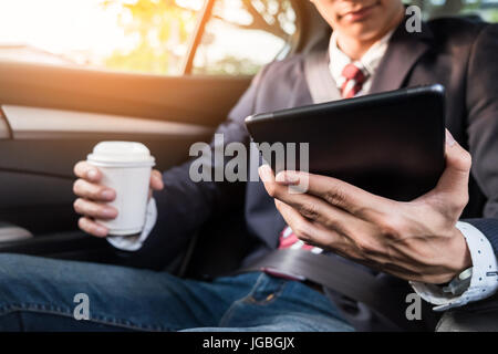 Giovane imprenditore bello lavorare nel retro della vettura e utilizzando un tablet o smart phone. Foto Stock