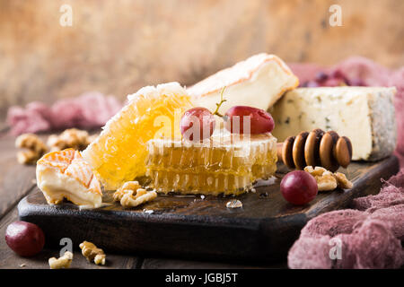 Favo di miele con formaggi assortiti, uva e noci sul vecchio tagliere di legno. Cibo sano concetto. Copia dello spazio. Foto Stock