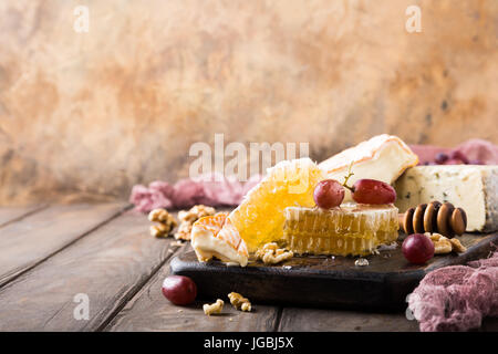 Favo di miele con formaggi assortiti, uva e noci sul vecchio tagliere di legno. Cibo sano concetto. Copia dello spazio. Foto Stock