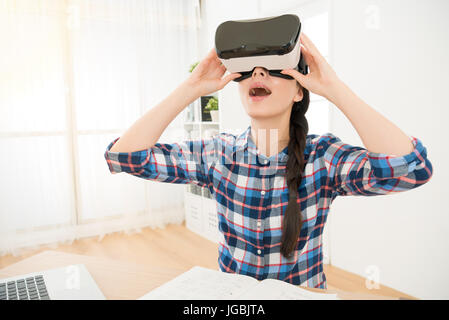 Close up di studente azienda VR-cuffia attrezzature e giocare online il gioco di godere di innovazione VIRTUAL REALITY 3d video sensazione incredibile seduto alla scrivania Foto Stock