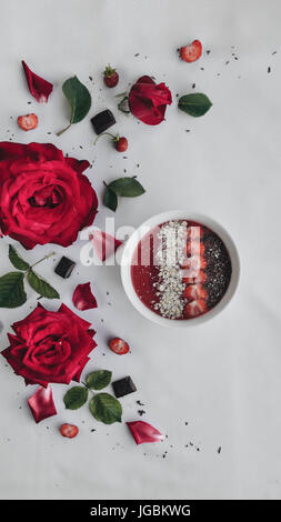 Al di sopra di vista del tè delizioso decorato con cioccolato e fragole sul tavolo pieno di rose rosse e petali di fiori. Foto Stock