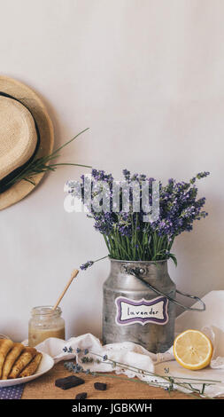 Composizione rustico della lavanda a secco nel secchio di ferro poste sul tavolo pieno di un pezzo di limone e il miele. Il cappello di paglia è appeso alla parete. Foto Stock