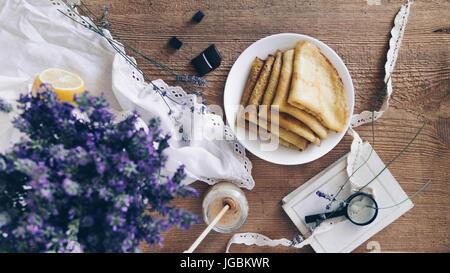 Al di sopra di vista della composizione rustico. Il profumo della lavanda secca, miele, lente di ingrandimento, pezzi di cioccolato e mattina piatto messo sul tavolo di legno. Foto Stock