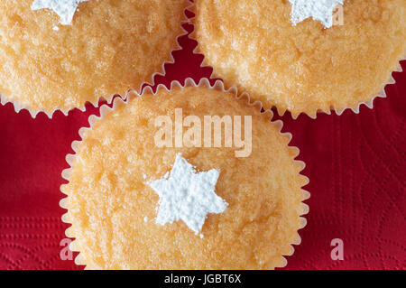 Tre tortini di vaniglia su un tovagliolo rosso sfondo, shot close up e overhead, decorato per il Natale con forme stellari spruzzata in bianco di zucchero a velo Foto Stock