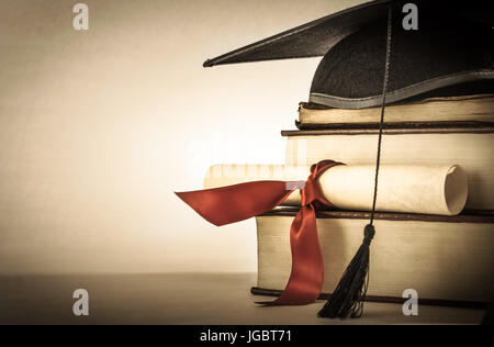 Un mortarboard e graduazione di scorrimento, legate con un nastro rosso, su di una pila di vecchi martoriata prenota con spazio vuoto a sinistra. Leggermente undersaturated con Foto Stock