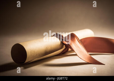 Una pergamena diploma scorrere, arrotolato con nastro rosso prevista in corrispondenza di un angolo obliquo. Elaborati per fornire un vintage o aspetto retrò. Foto Stock