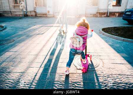 Bambina con capelli biondi corse su scooter Foto Stock