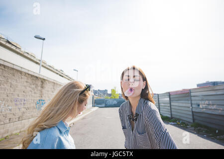 Due belle giovani donne a giocare con bubble gum outdoor in città - la felicità, allontanarsi da tutto e da tutti, il concetto di amicizia Foto Stock