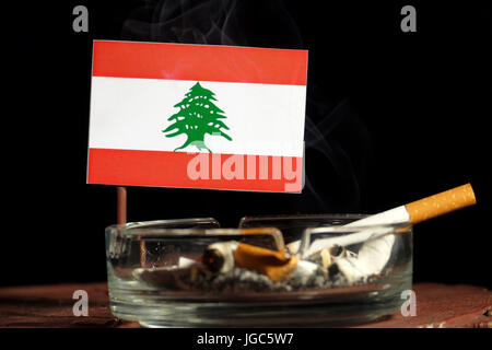 Bandiera libanese con la sigaretta accesa nel posacenere isolati su sfondo nero Foto Stock