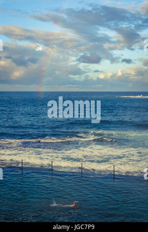 Rainbow e uomo di nuoto in Wylies bagni, un pool di marea nei pressi di Coogee Beach, sobborghi Orientali, Sydney, Australia Foto Stock