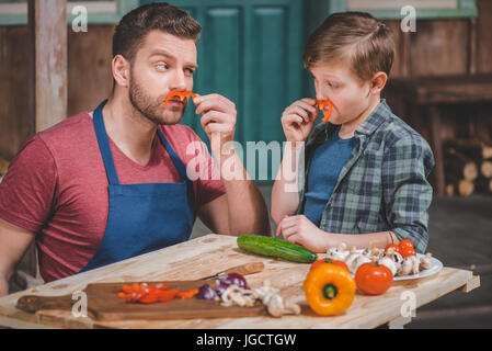 Padre nel grembiule e carino piccolo figlio di divertirsi con pepe baffi, papà e figlio concetto di cucina a vista Foto Stock