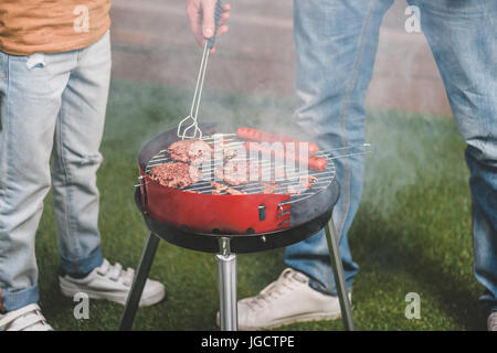 Vista parziale di padre e figlio la cottura di hamburger di manzo su barbecue Foto Stock