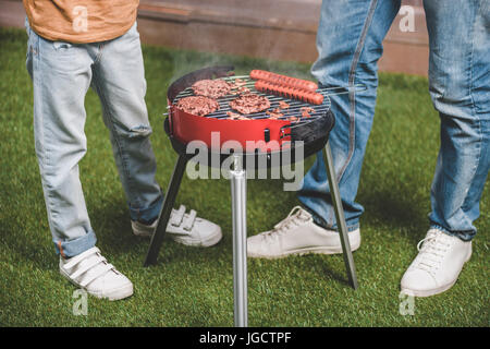 Vista parziale di padre e figlio la cottura di hamburger e hot dog salsicce sul barbecue Foto Stock