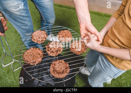 Vista parziale di padre e figlio la cottura di hamburger di manzo su barbecue Foto Stock