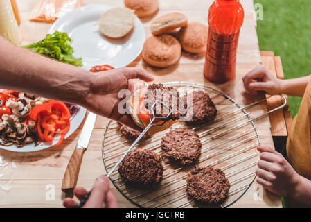 Vista parziale di papà e figlio la cottura della carne Hamburger insieme Foto Stock