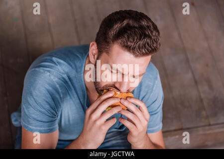 Angolo di alta vista del giovane uomo mangiare hamburger Foto Stock