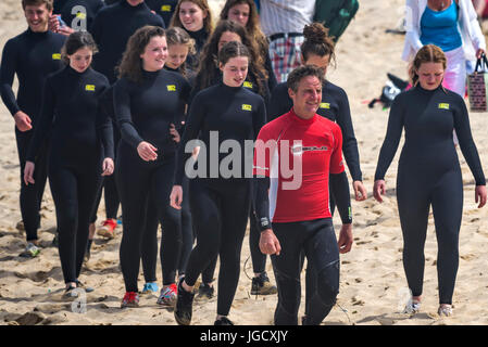 Una scuola di surf istruttore conduce a un gruppo di novizie attraverso Fistral Beach in Newquay, Cornwall. Foto Stock