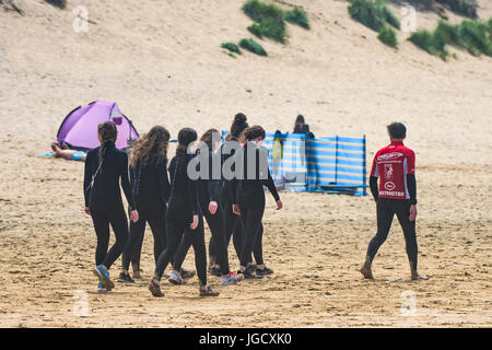 Una scuola di surf istruttore conduce a un gruppo di novizie attraverso Fistral Beach in Newquay, Cornwall. Foto Stock