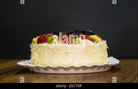 Deliziosa crema bianco intero torta al cioccolato con frutta sulla parte superiore su uno sfondo scuro Foto Stock