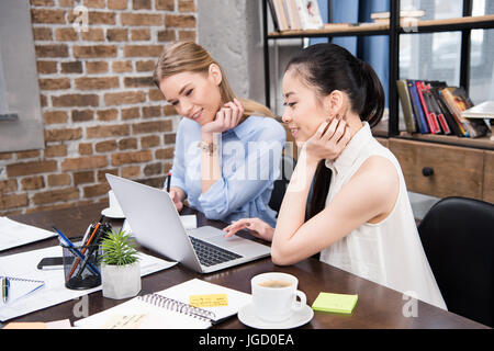 Sorridente imprenditrici multiculturale lavora con laptop e seduti al posto di lavoro Foto Stock