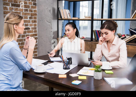 Tre imprenditrici multiculturale lavorando e discutendo il progetto al lavoro in ufficio moderno Foto Stock