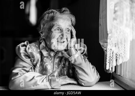 Signora anziana si siede al tavolo e guardando fuori dalla finestra. Foto in bianco e nero. Foto Stock