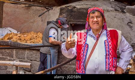 Pisac Perù uomo che indossa un colorato chollo bake empanadas in un antico forno horno in Perù, Sud America. Foto Stock