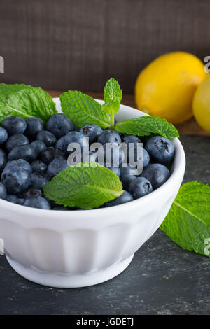 Sani frutti - mirtilli e il giallo dei limoni in una ciotola bianco - crudo, deliziosi e nutrienti, alimenti funzionali Foto Stock