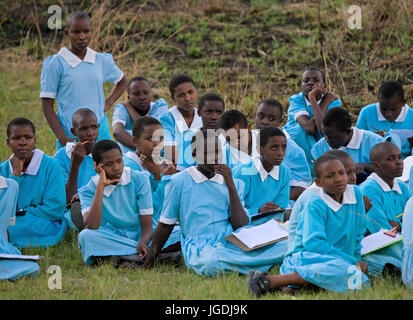 Kenia Masai Mara - Luglio 18, 2008: scuola gli studenti sedersi sulla terra e aspettare il bus di scuola. Foto Stock