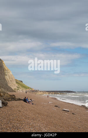 Costiera vista mare con scogli e persone in un giorno nuvoloso tra riva di ghiaia linea di spiaggia Eype, Symmondsbury, vicino a Bridport, Dorset, Regno Unito. Foto Stock